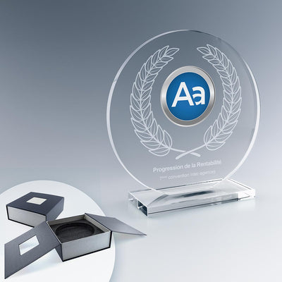 Trophée rond en verre sur socle avec gravure laser et logo en couleur, à côté de son écrin cadeau noir
